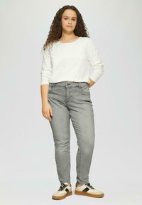 Graue Jeans aus Denim mit schlanker Passform, kombiniert mit einem weißen Langarmshirt und beigen Sneakers mit dunklen Akzenten. Glatte Textur im gesamten Design.