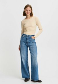 Beige långärmad ribbad topp som matchas med bredbeniga blå denimjeans. Jeansen har hög midja och en blekt finish med framfickor.