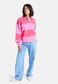 Rosa og lyserosa stripete genser med hvit krage, med en avslappet passform. Bært sammen med lyseblå vide jeans og hvite sneakers.