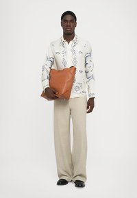 Hvid skjorte med blå blomstertryk, beige bukser og en brun lædertaske. Tasken er blød og overdimensioneret med et minimalistisk design.
