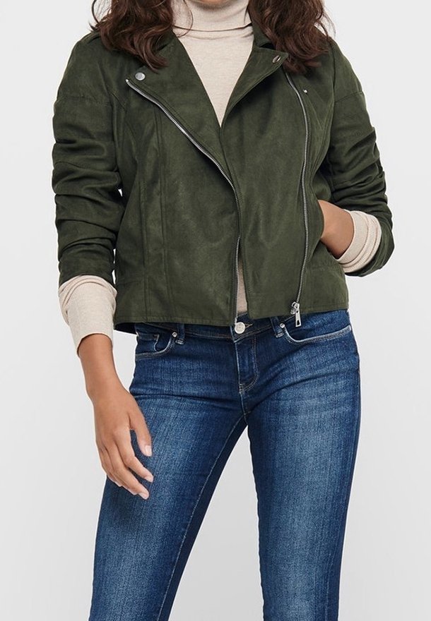 Veste en daim vert olive avec un design ajusté, fermeture zippée et détails d'épaulettes, associée à un col roulé beige et un jean bleu.