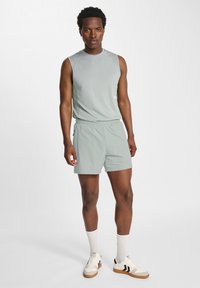 Ljusgrön ärmlös sporttopp i kombination med matchande shorts; tyget verkar slätt och lättviktigt, med en elastisk midja. Avslappnade skor visas.