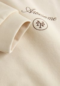 Kreemivärvi särk, millel on sooniknader, ja keskel pruunilt tikitud kiri "Lahe" ning ringikujuline logo.