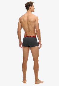 Bañadores de boxeador grises con una cinturilla elástica que presenta la marca "SUPERDRY" en rojo; diseño ajustado y textura suave.