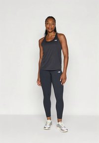 Czarny sportowy top na ramiączkach i legginsy w połączeniu z srebrno-białymi sneakersami, charakteryzujące się dopasowanym krojem i akcentami z logo New Balance.