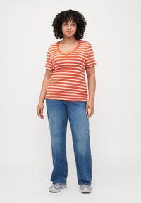 Orange and white striped short-sleeve V-neck t-shirt paired with blue flared jeans and gray sneakers. Smooth cotton fabric.