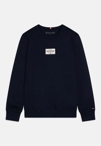Felpa blu navy con scollo rotondo, tessuto strutturato, una toppa rettangolare bianca con la scritta "Tommy HILFIGER" e piccoli accenti con il logo sulle maniche.