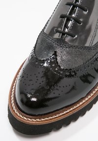 Chaussure en cuir verni noir avec des détails de brogue, des accents en daim noir texturé, un bout arrondi et une semelle en caoutchouc épaisse avec un bord cousu.