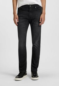 Jeans in denim nero con una vestibilità slim, design a cinque tasche, leggera scoloritura e gamba dritta, abbinati a sneaker nere con suola bianca.