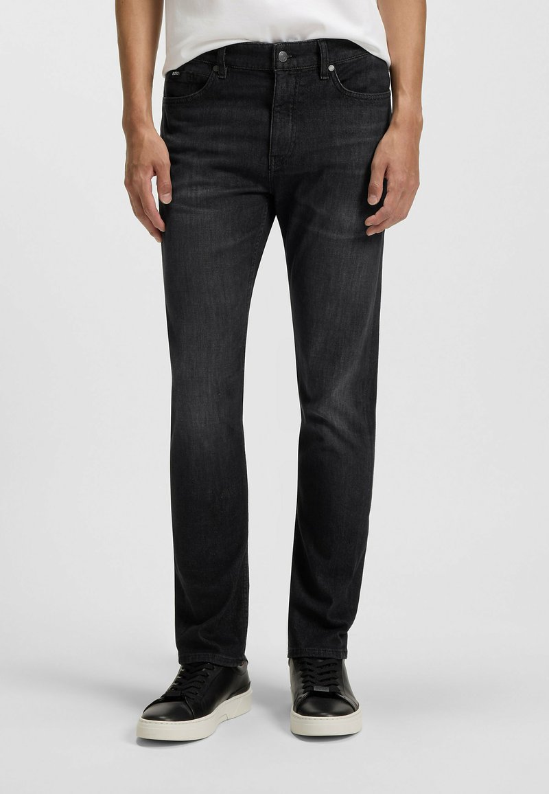 Jeans in denim nero con una vestibilità slim, design a cinque tasche, leggera scoloritura e gamba dritta, abbinati a sneaker nere con suola bianca.