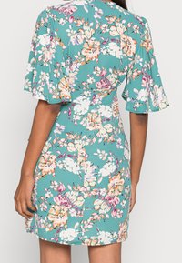 Vestido floral con fondo verde azulado y flores rosas, blancas y naranjas. Mangas cortas acampanadas y cintura ajustada con dobladillo recto.