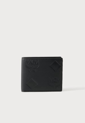 Portefeuille bifold en cuir noir embossé de logos MCM et de formes en diamant, présenté fermé sur un fond gris clair.