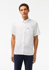 Camicia di lino bianca a maniche corte con colletto button-down, dotata di taschino sul petto e di un piccolo logo verde sul lato sinistro.