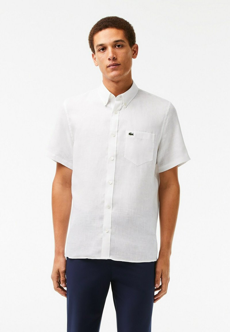 Camicia di lino bianca a maniche corte con colletto button-down, dotata di taschino sul petto e di un piccolo logo verde sul lato sinistro.