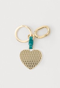 Χρυσό μπρελόκ σε σχήμα καρδιάς με υφή, προσαρτημένο σε χρυσούς κρίκους και ένα τυρκουάζ δερμάτινο λουράκι σε λευκό φόντο.