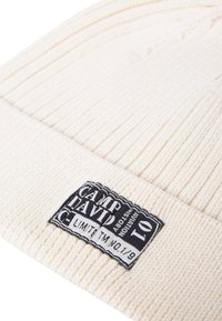 Cream knitted beanie with ribbed texture and a prominent black label featuring "CAMP DAVID" and "LIMITED TM NO. 1/9" details.