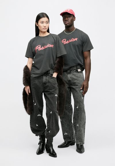 Svarta grafiska t-shirts med ordet "Passion" i rött, kombinerade med grå jeans med kaninmönster. En modell håller i en accessoar av fuskpäls.