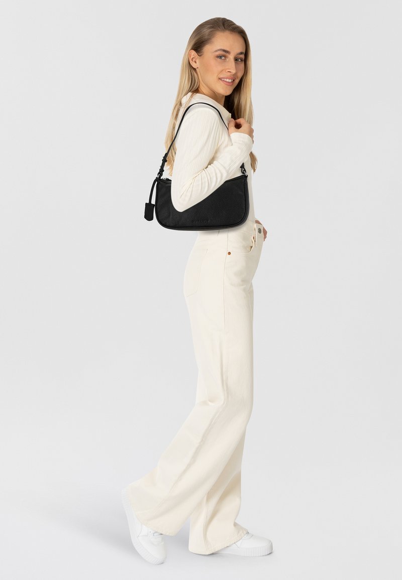 Borsa nera in tessuto strutturato con tracolla regolabile, abbinata a una maglietta a maniche lunghe color crema e pantaloni larghi chiari, stile casual.