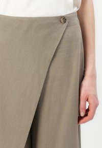 Beige Wickelrock aus strukturiertem Stoff, mit Knopfverschluss an der Taille und überlappenden Vorderteilen.