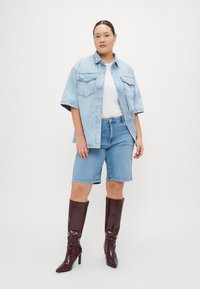 Svetlo modra denim oversized srajca s kratkimi rokavi, ujemajoča se s svetlo modrimi denim kratkimi hlačami in visokimi škornji v burgundski barvi z visokim sijajem.