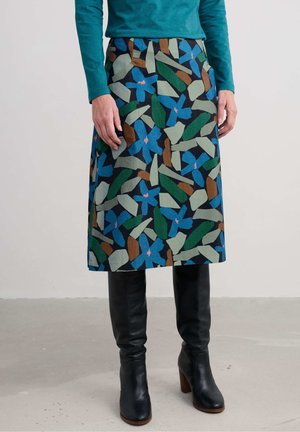 Multicolored A-line skirt featuring a leaf pattern in green, blue, and brown on a dark background; worn with knee-high black leather boots.