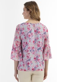 Blusa floreale con sfondo azzurro chiaro, rose rosa e viola, maniche arricciate e chiusura con bottone sul retro.