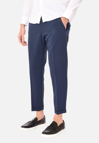 Pantaloni tapered blu navy realizzati in tessuto morbido, dotati di tasche laterali e un design pulito. Indossati con scarpe slip-on nere.