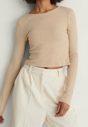 Beige Langarmoberteil aus geripptem Stoff mit rundem Ausschnitt und cropped Design, kombiniert mit weißen hoch taillierten Hosen.