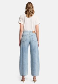 Jasnoniebieskie dżinsy typu wide-leg z wysokim stanem, z skórzaną metką z tyłu i postrzępionymi brzegami. W połączeniu z gładką białą koszulką.