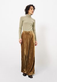 Gestreepte coltrui in groen en crème, gecombineerd met wijde, bruine fluwelen broek. De broek heeft een hoge taille en een zachte textuur.