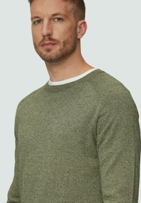 Zielony sweter o fakturze z okrągłym dekoltem i białym akcentem przy kołnierzu. Posiada rękawy raglanowe oraz dopasowany krój.