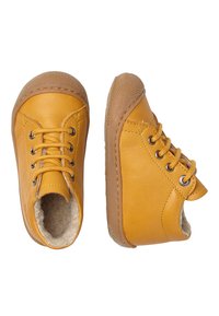 Žluté kožené boty se šněrováním, kulatou špičkou a opálenou gumovou podrážkou. Vnitřní fleece podšívka viditelná u otvoru, zdobená očky.