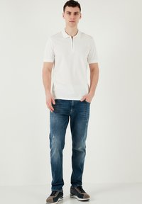 Vit kortärmad polo med dragkedja, matchad med blå slitna jeans och grå sneakers med marinblå detaljer. Minimalistisk design.