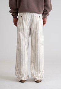 Vide bukser laget av lett stoff med kremfargede og beige vertikale striper. Har baklommer og brune knappdetaljer.