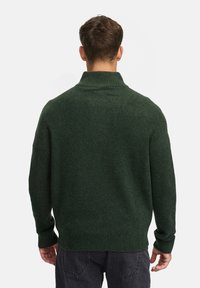 Donkergroene gebreide trui met een hoge kraag, geribbelde manchetten en zoom, met een zachte textuur en een relaxte pasvorm.