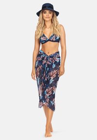 Granatowy bikini z kwiatowym wzorem w odcieniach różu i niebieskiego, w zestawieniu z luźną, przezroczystą sarongiem zawiązanym w talii. Modelka nosi granatowy kapelusz.