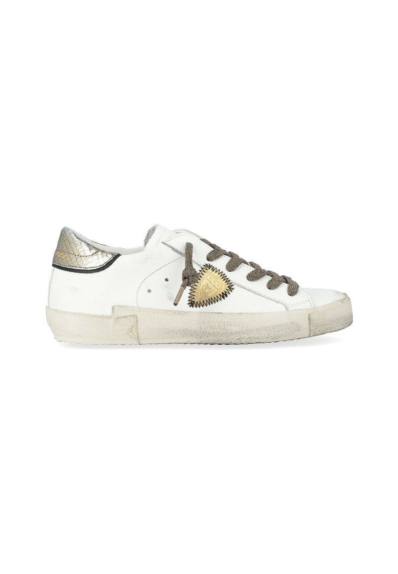 Des baskets blanches en cuir avec un talon doré métallique, des lacets gris texturés et un patch triangulaire doré sur le côté. Semelle usée visible.