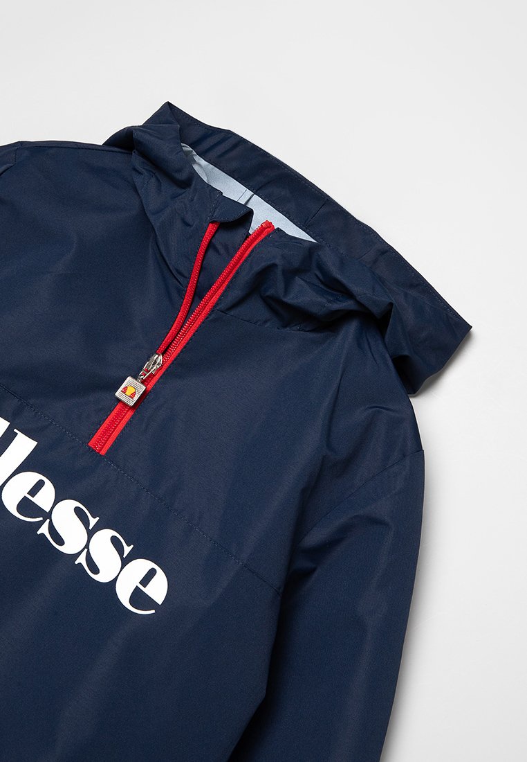 Chaqueta azul marino con capucha, cremallera frontal roja y el logo blanco de "ellesse" en el pecho.
