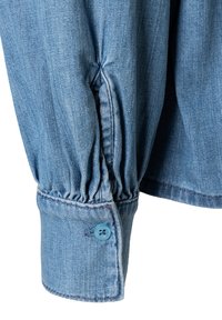 Blauwe denim shirt met een gathered detail bij de mouwzoom en een lichtblauwe knop. Gladde textuur met zichtbare stikselaccenten.