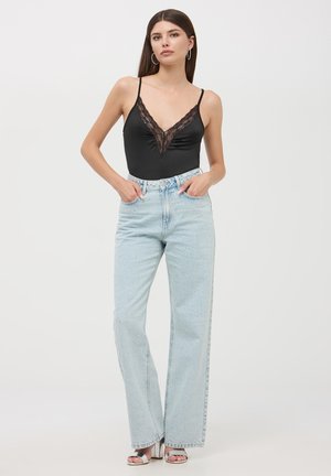 Body in pizzo nero con bordi in pizzo abbinato a jeans a vita alta di un azzurro chiaro, dritti. Calzature: decolleté aperti argentati.