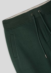 Zielone dresowe spodnie o miękkiej teksturze, z elastycznym pasem, sznurkiem ściągającym i bocznymi kieszeniami. Prosty, funkcjonalny design.