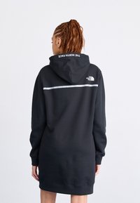Svart hoodie-klänning med lång ärm, med "The North Face" i vitt på huvan och ett reflexband över ryggen.