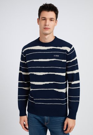 Maglione lavorato a maglia blu navy con strisce orizzontali bianche, collo a barcos, polsini e orlo a coste; presenta il logo "GUESS" sul davanti.