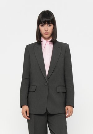 Mørkegrå skreddersydd blazer med en enkelt knapp, notched slag og to frontlommer, båret over en lys rosa skjorte med krage.