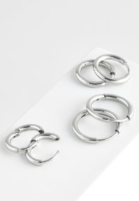 Zwei Paar silberne Creolen mit glatter, glänzender Oberfläche; ein kleines und ein größeres Paar, auf einer weißen Oberfläche präsentiert.