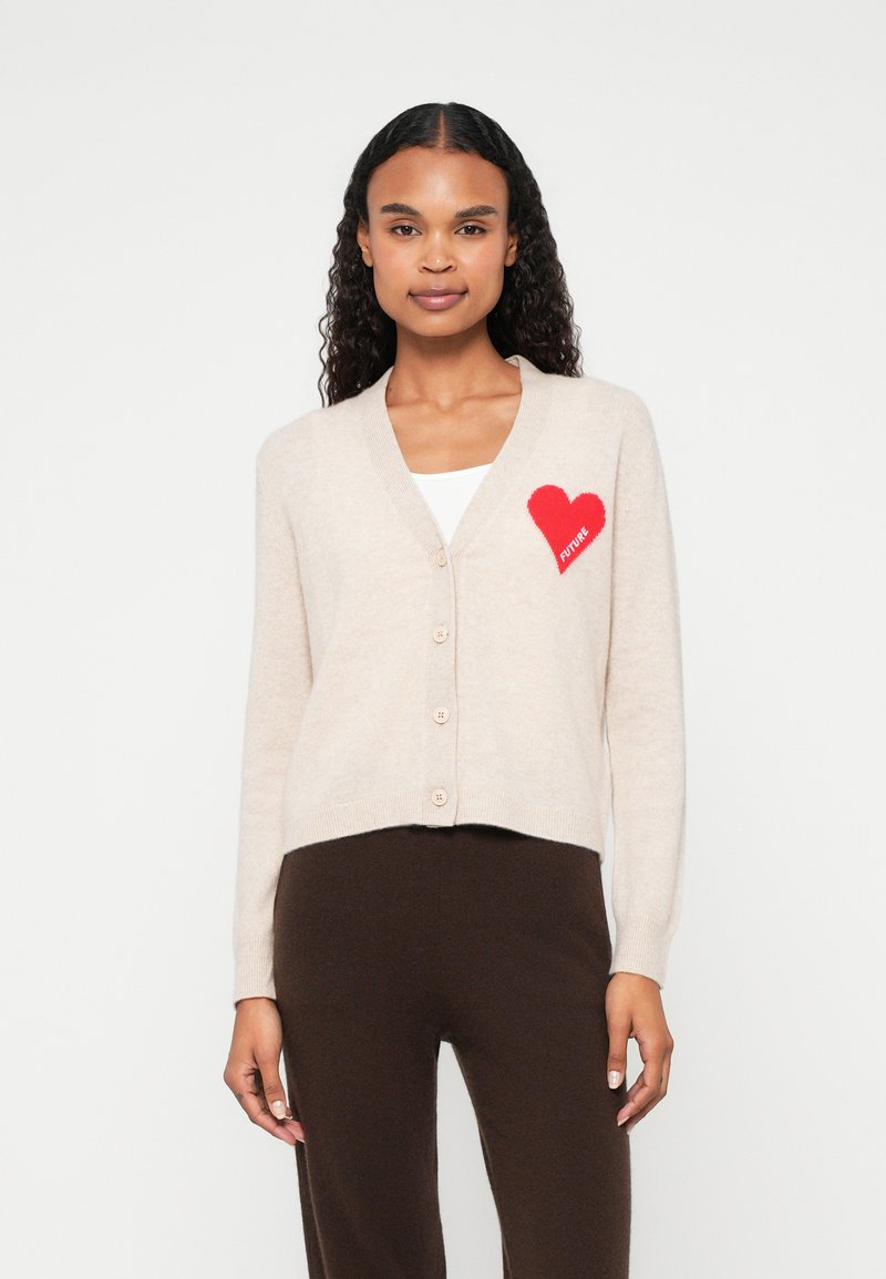 Beige kardigán, puha anyagból, V nyakkivágással, öt gombbal és egy piros szívvel, ami a bal mellen található, rajta a "FUTURE" felirattal.