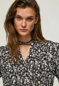 Blusa a fantasia floreale in nero, grigio e bianco, con scollatura a V e dettaglio con fiocco, maniche corte a sbuffo e tessuto leggero.