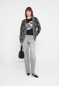 Grå fuzzy cardigan med sorte leopardprikker, båret over en svart grafisk t-skjorte, kombinert med lyse grå jeans og svarte spisse hæler.