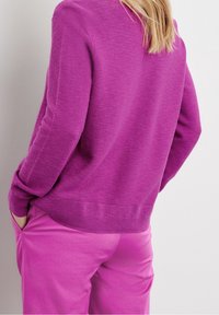 Purple knitted sweater with a ribbed hem and cuffs, paired with pink pants. The fabric has a soft, textured appearance.