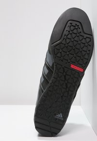 Czarna podeszwa buta sportowego z teksturowanym gumowym wzorem, z czerwonym akcentem "TRAXION" i trzema czarnymi paskami po bokach.